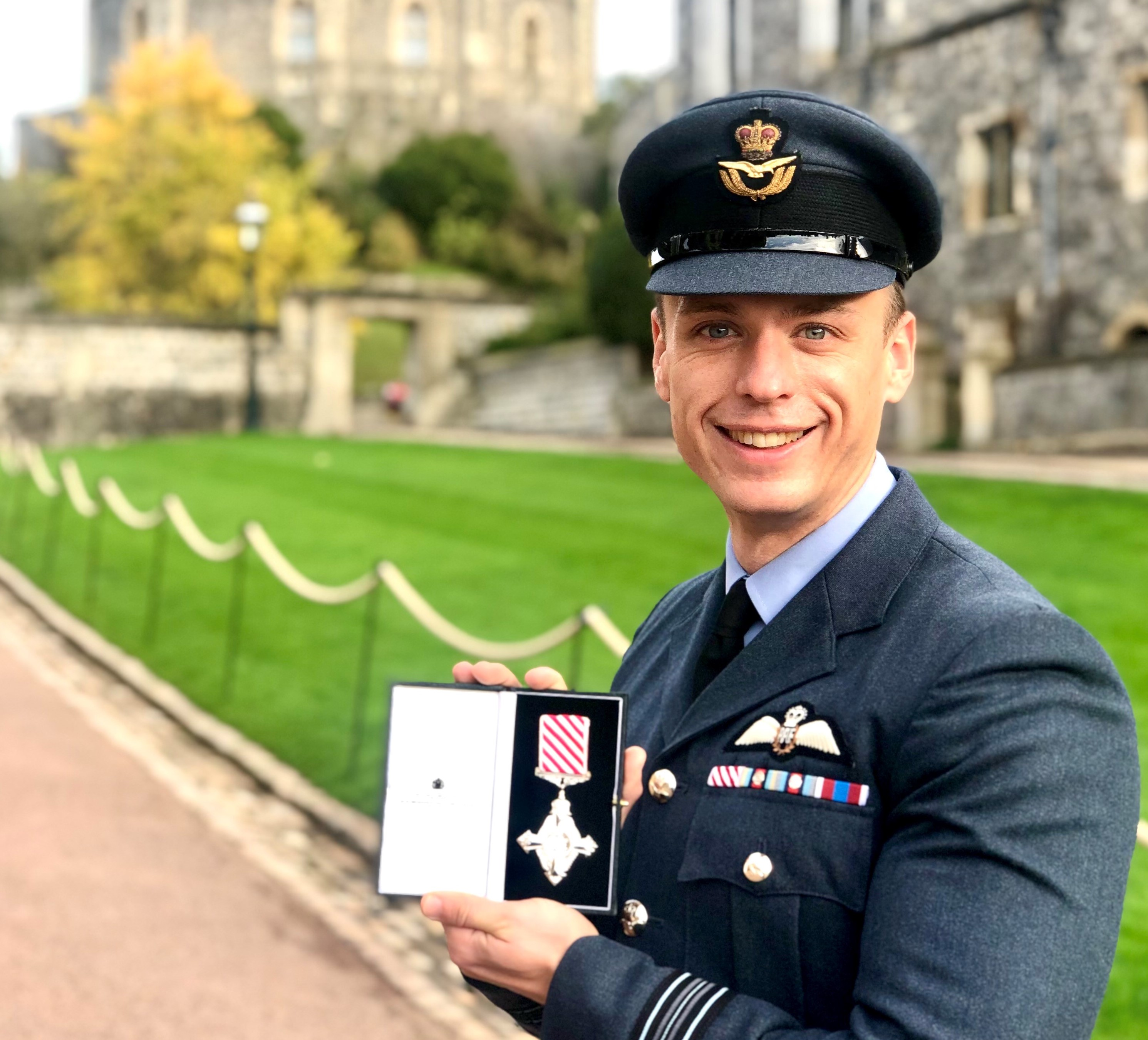Image shows RAF aviator holding medal outside Windsor Castle.
